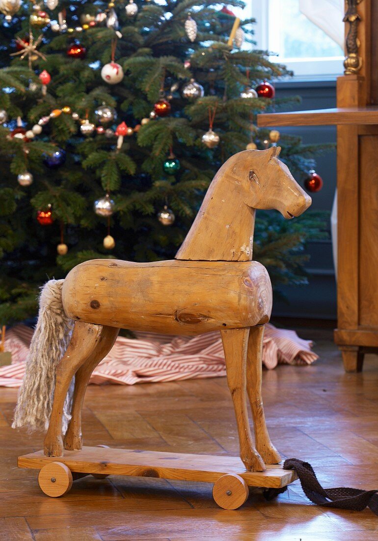 Historisches Weihnachtsspielzeug: Antikes Holzpferd zum Ziehen vor einem Weihnachtsbaum