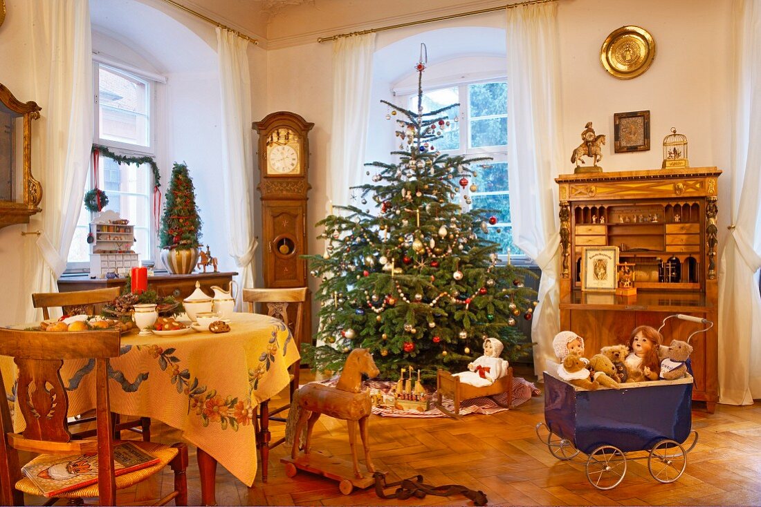 Klassisch geschmückter Weihnachtsbaum und historisches Spielzeug im Wohnraum mit antiken Möbeln
