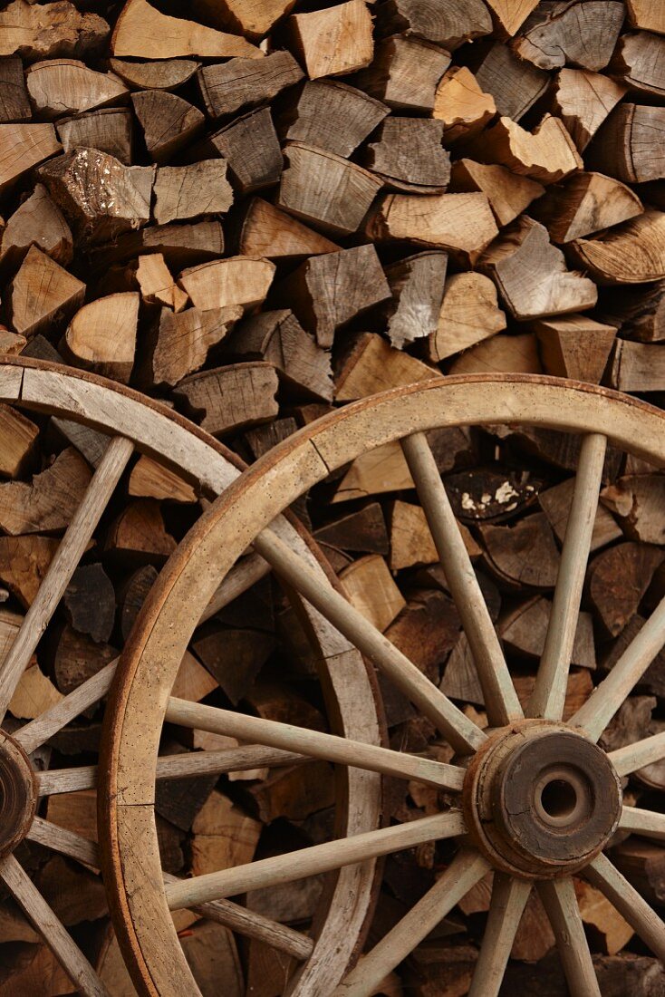 Two old wooden wagon wheels in front of stacked firewood