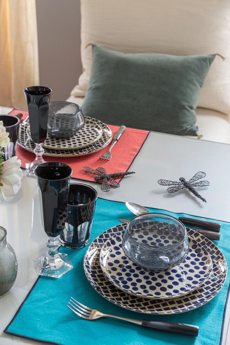 Gedeckter Tisch mit bunten Sets, gepunkteten Tellern und schwarzen Gläsern