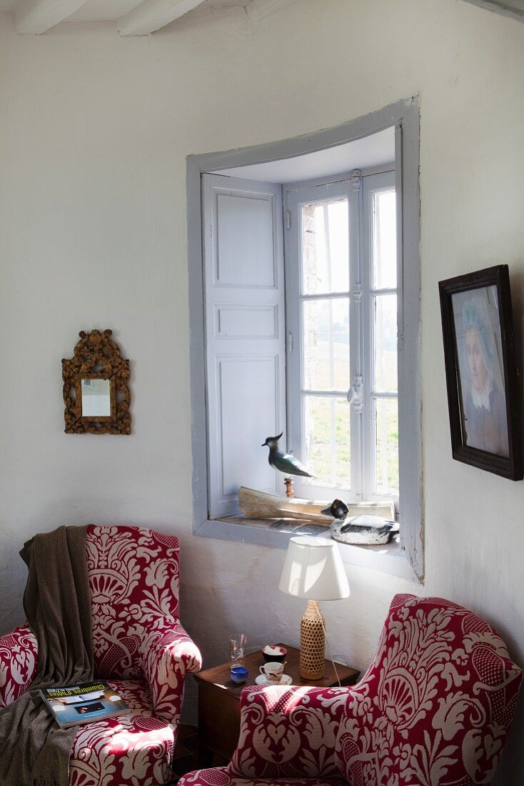 Armlehnsessel mit rot-weißem Ornamentmuster vor Sprossenfenster