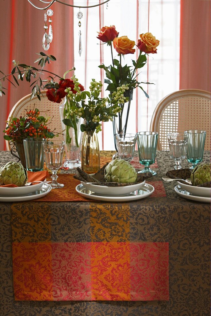 Herbstlich gedeckter Tisch dekoriert mit Rosen, Beeresträussen und Artischocken