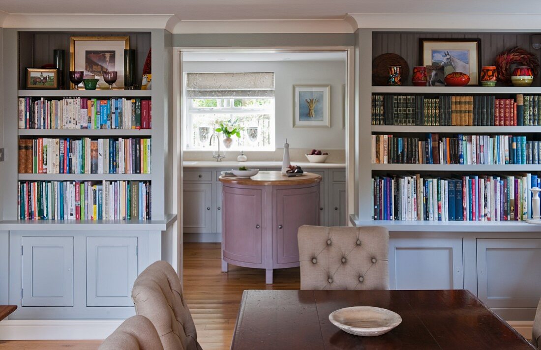 Blick vom Esszimmer mit Bücherwand in ländliche Küche mit Kassettenfronten in Pastelltönen