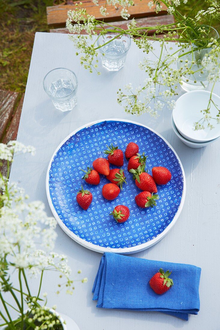 Eine blaue Schale mit frischen Erdbeeren auf dem Gartentisch