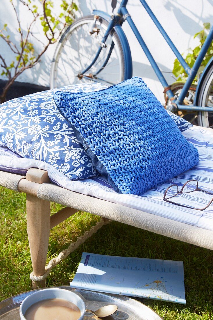 Cushion with blue knitted cover on camp bed in garden
