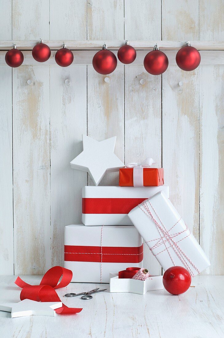 Rot-weiß verpackte Geschenke vor einer Bretterwand mit Christbaumkugeln