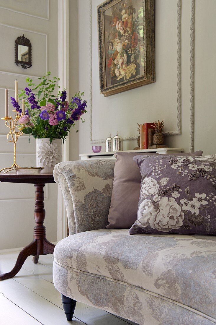Geblümtes Sofa mit Blumenkisten, dahinter Vase mit Blumenstrauß und ein Blumen-Gemälde