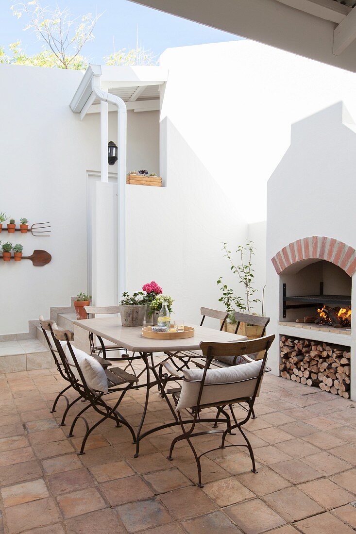 Mediterraner Innenhof mit gemauertem Grill, Tisch und Stühlen aus Metall
