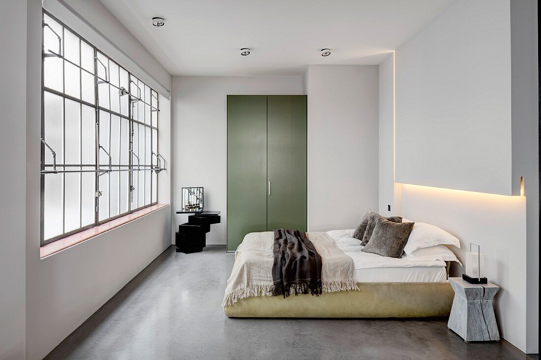 Bedroom in industrial loft apartment with concrete floor and factory windows