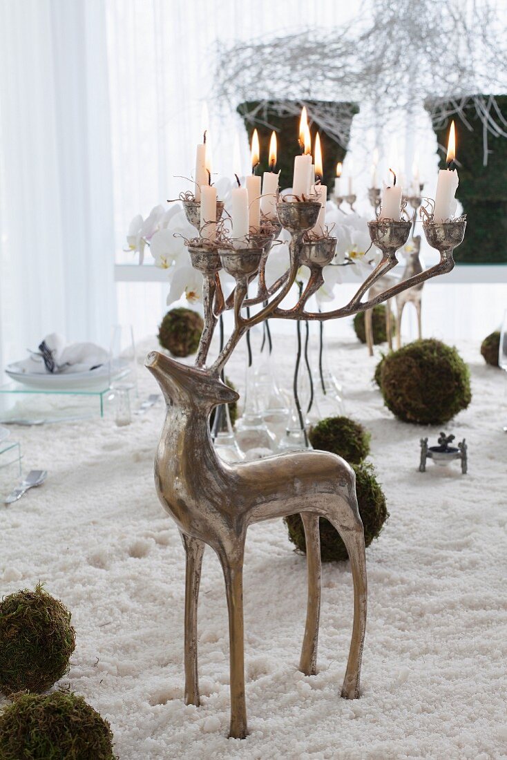 Silberner Kerzenständer in Form eines Hirschs mit brennenden Kerzen im Geweih auf Kunstschnee
