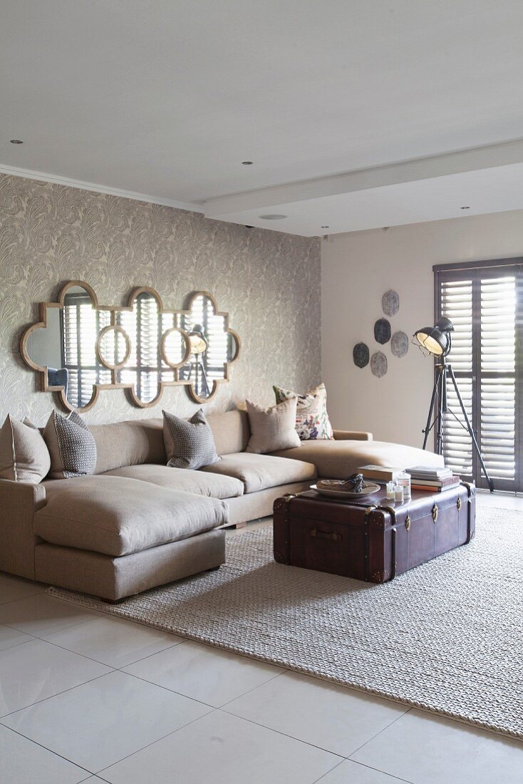 Wohnzimmer in Sandfarben mit Ornament-Spiegel und Überseekoffer als Couchtisch