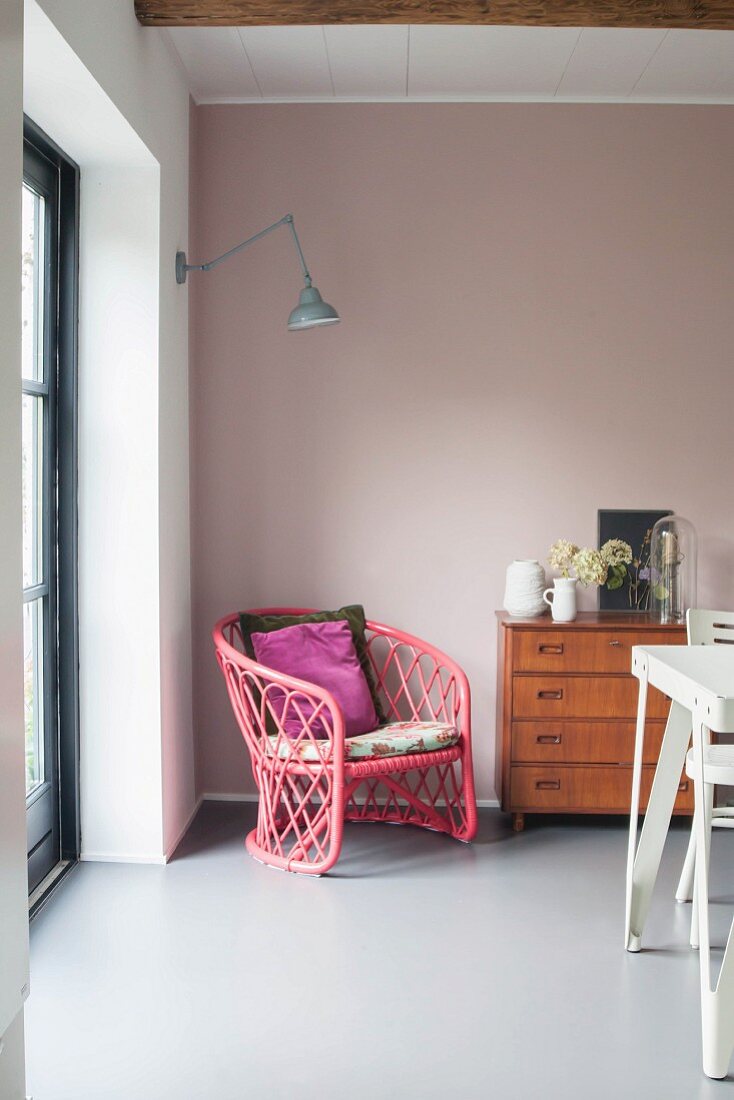 Pink rattan armchair and retro chest of drawers against pink wall