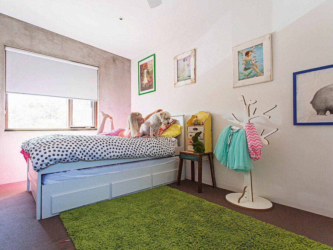 Mädchen mit Hund auf Bett im Kinderzimmer mit Betonwand und Flohmarktartikeln