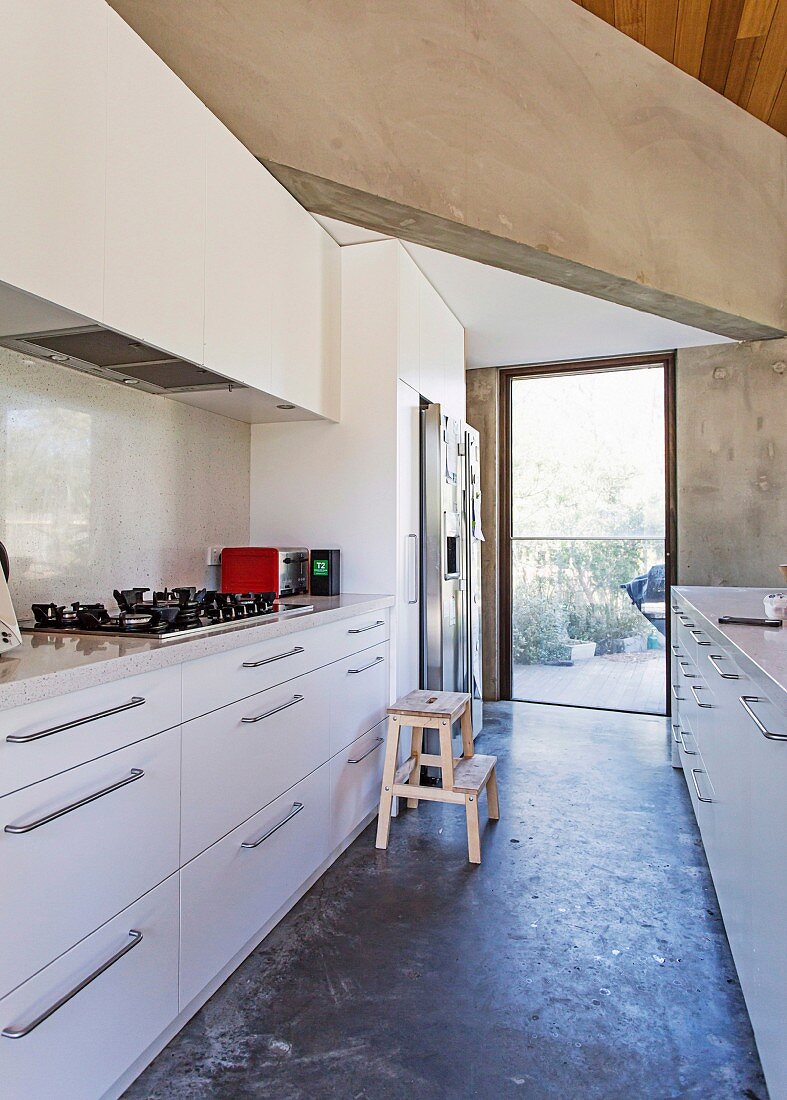 View of white designer fitted kitchen units and massive concrete beams, garden view