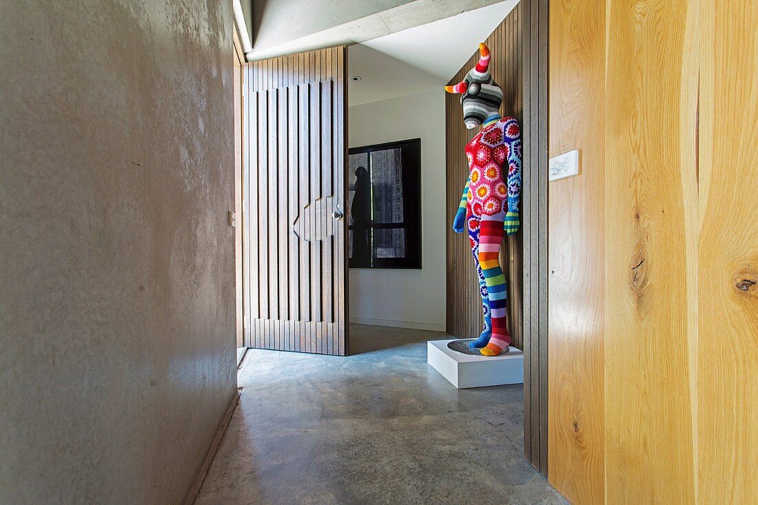 Bunt umhäkelte Kunstfigur im Eingangsbereich mit Betonboden und Betonwand