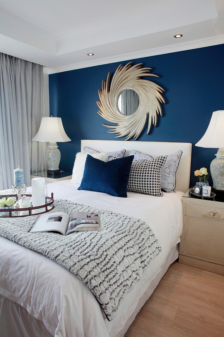 Elegantes Schlafzimmer mit dunkelblauer Wand und Spiegel über dem Bett