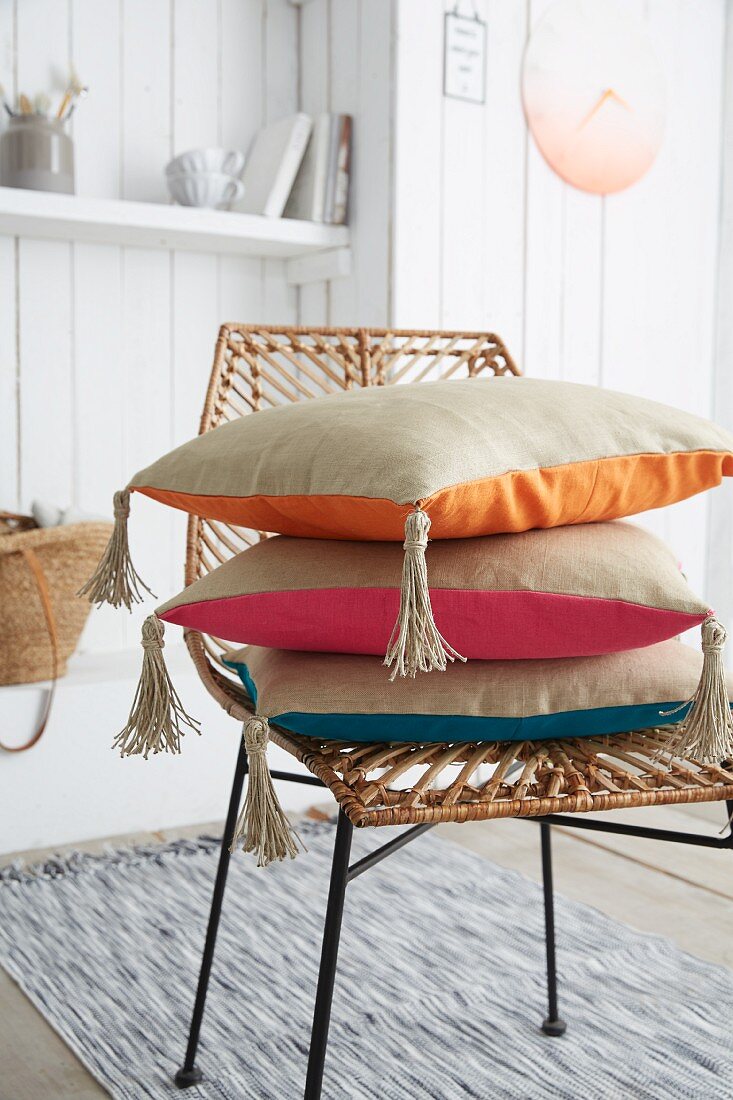 Stacked cushions with hand-sewn covers and tassels on wicker chair