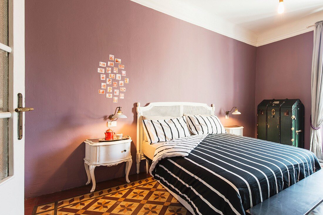 Antique bed, black and white striped bed linen and arrangement of photos on mauve wall in elegant bedroom