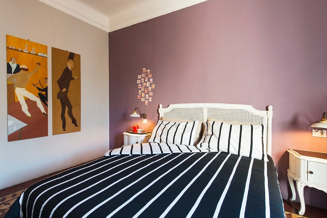White double bed with black and white striped bed linen against mauve wall