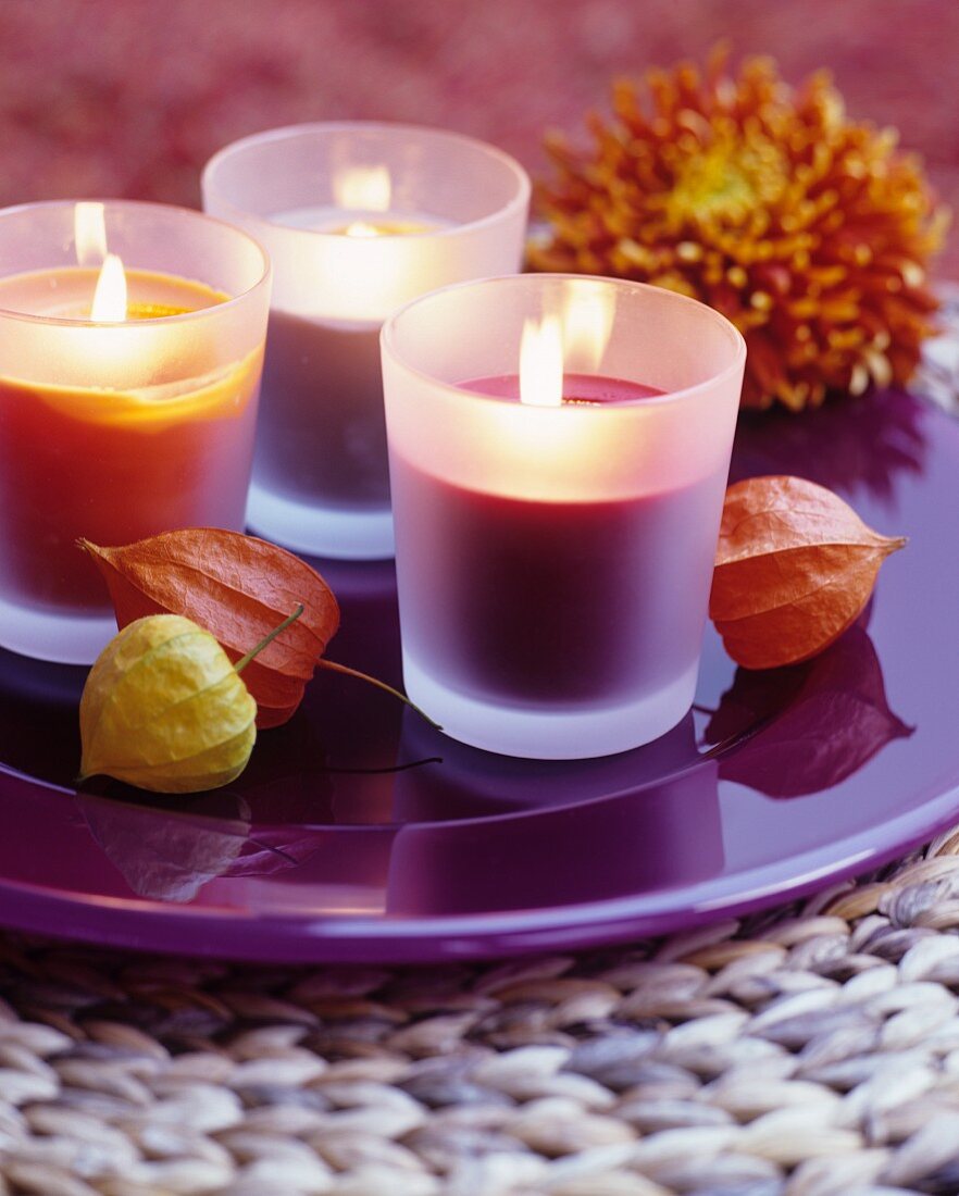 Brennende Duftkerzen auf lilafarbenem Teller mit Lampionblumen dekoriert