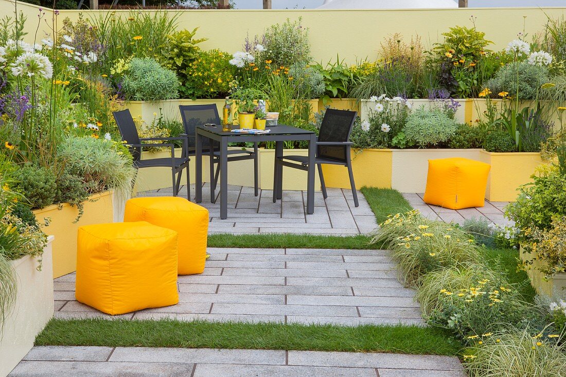 Seating area in courtyard garden with terraced flowerbeds in various shades of yellow