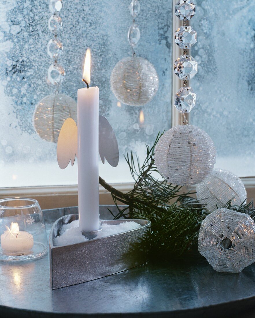 weiße brennende Kerze in weihnachtlich silber-weiß schimmerndem Ambiente
