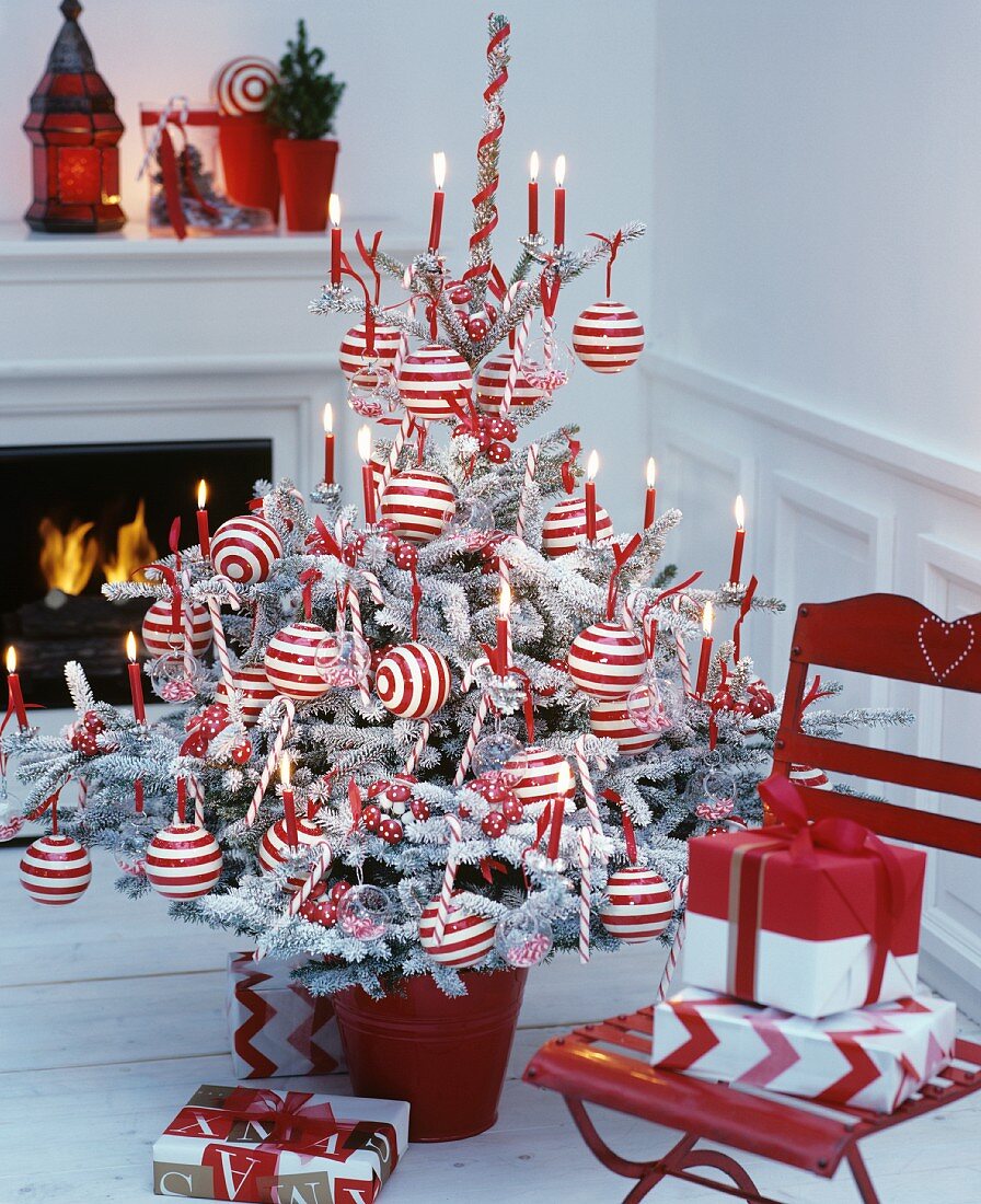 Christmas tree decorated with red and white striped baubles and red lit candles in front of fireplace