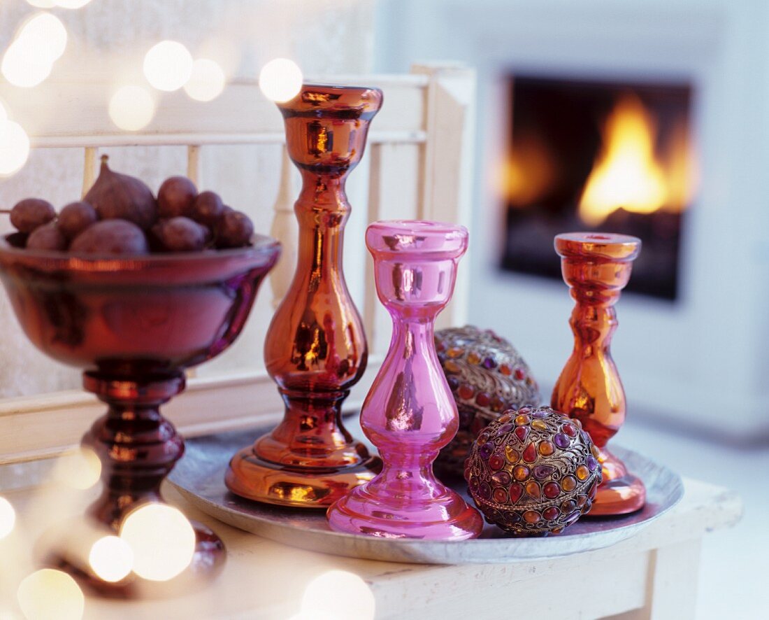 Glänzende, farbige Kerzenständer mit kunstvoll verzierten Kugeln auf Tablett neben Obstschale