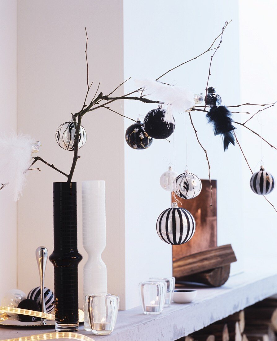 Elegant baubles and bird ornaments on bare branch in black vase