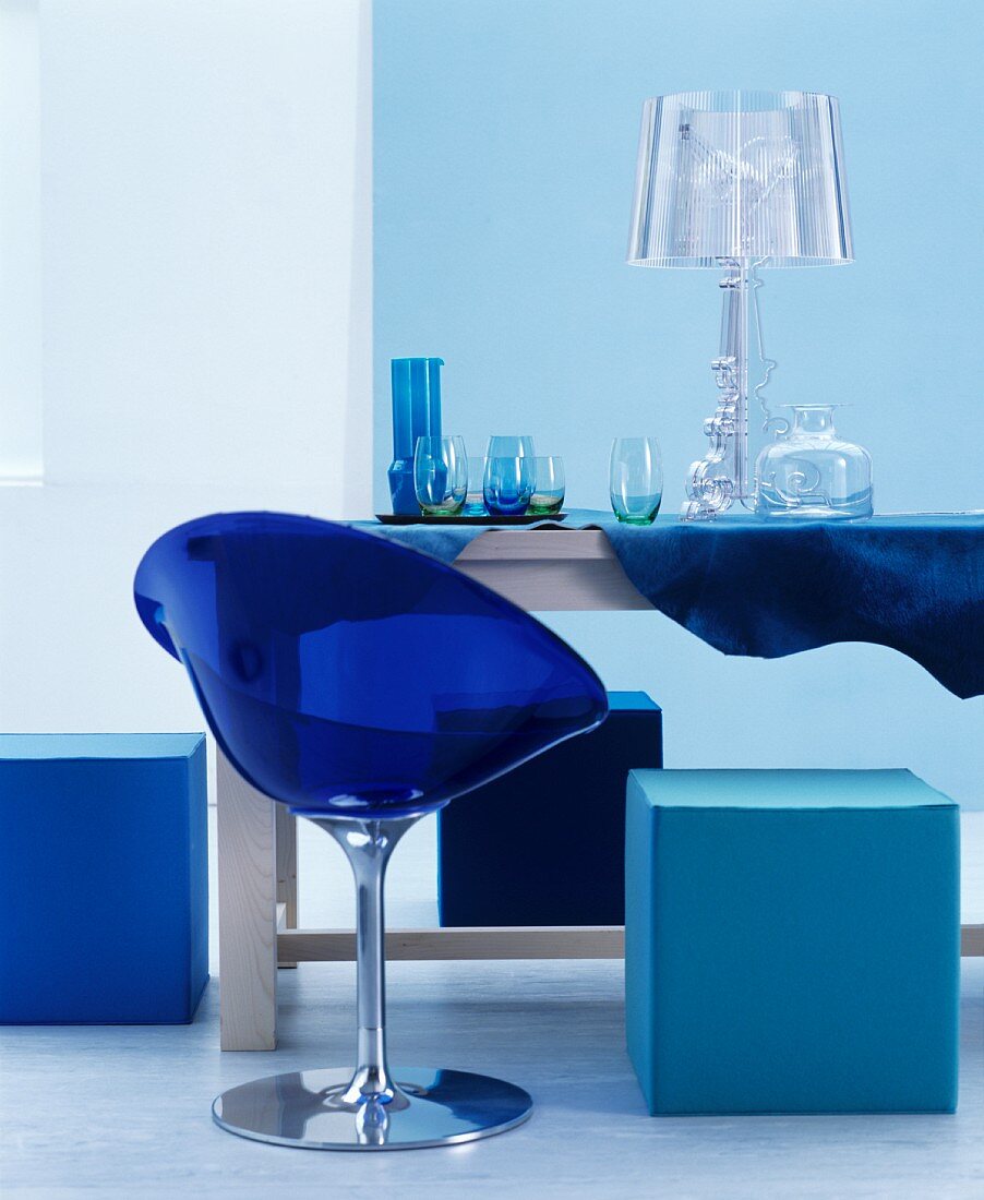 Blauer Plastikstuhl und Sitzwürfel um einen Tisch mit Gläsern und Leuchte