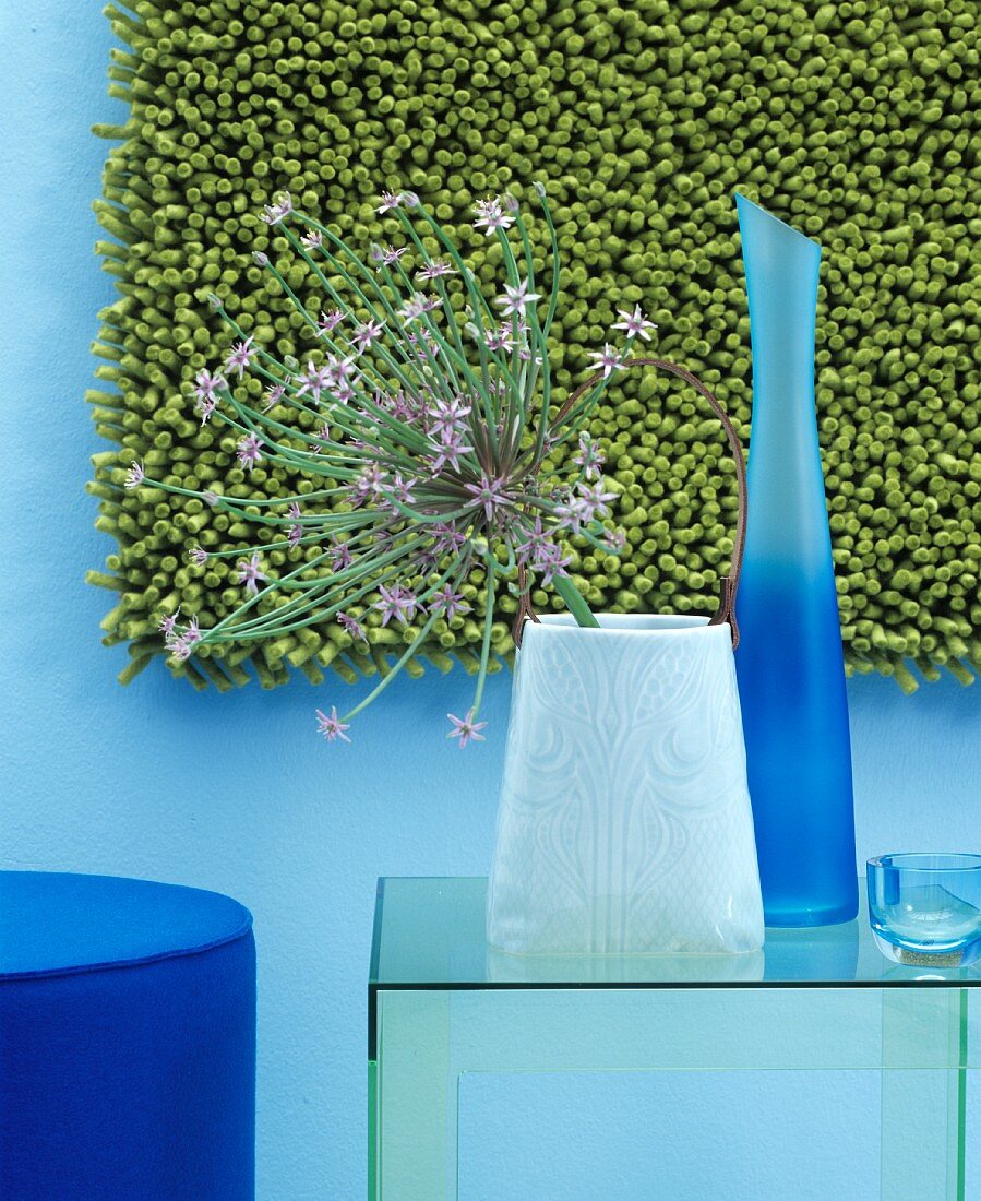 Zierlauchblüte und zwei Vasen vor einem grünen Teppich an der Wand