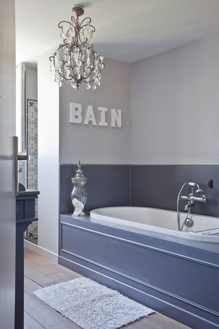 Elegant bathroom in shades of grey with panelled bathtub and chandelier