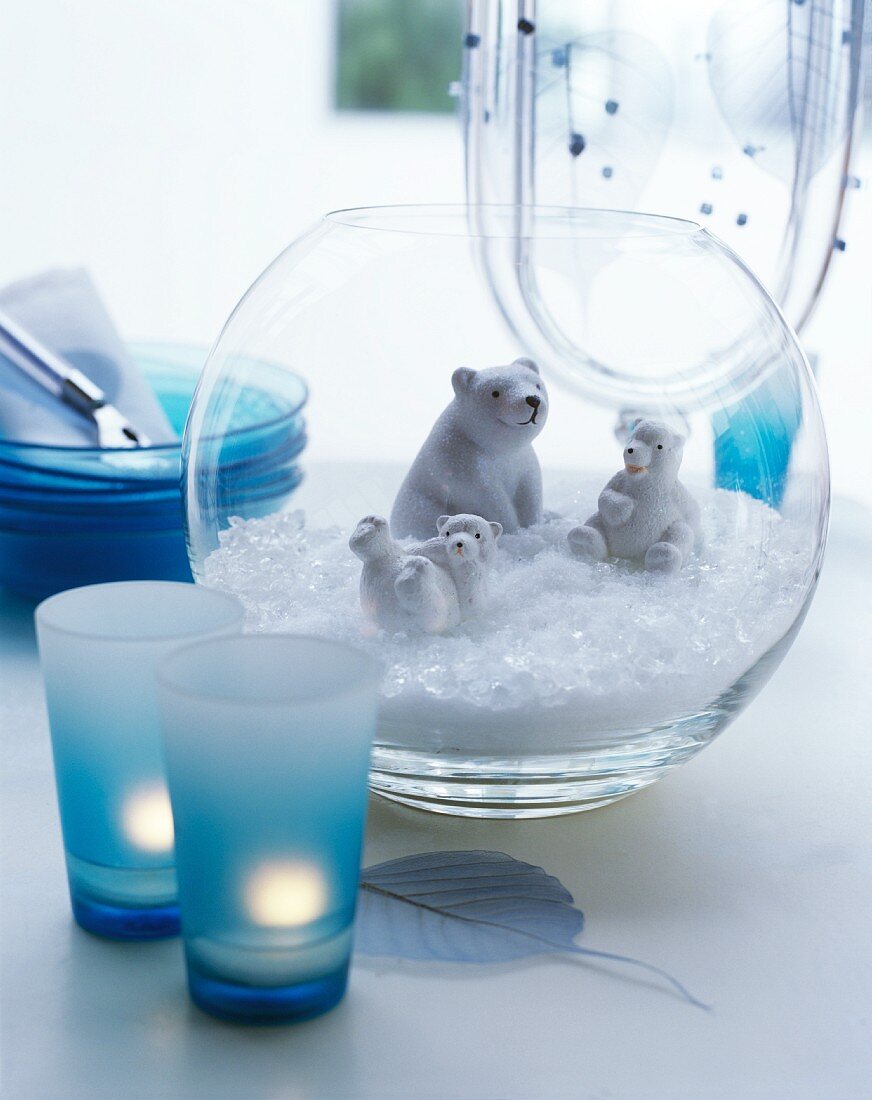 Eisbärfiguren mit Kunstschnee in Glasvase und blaue Gläser mit Teelichtern