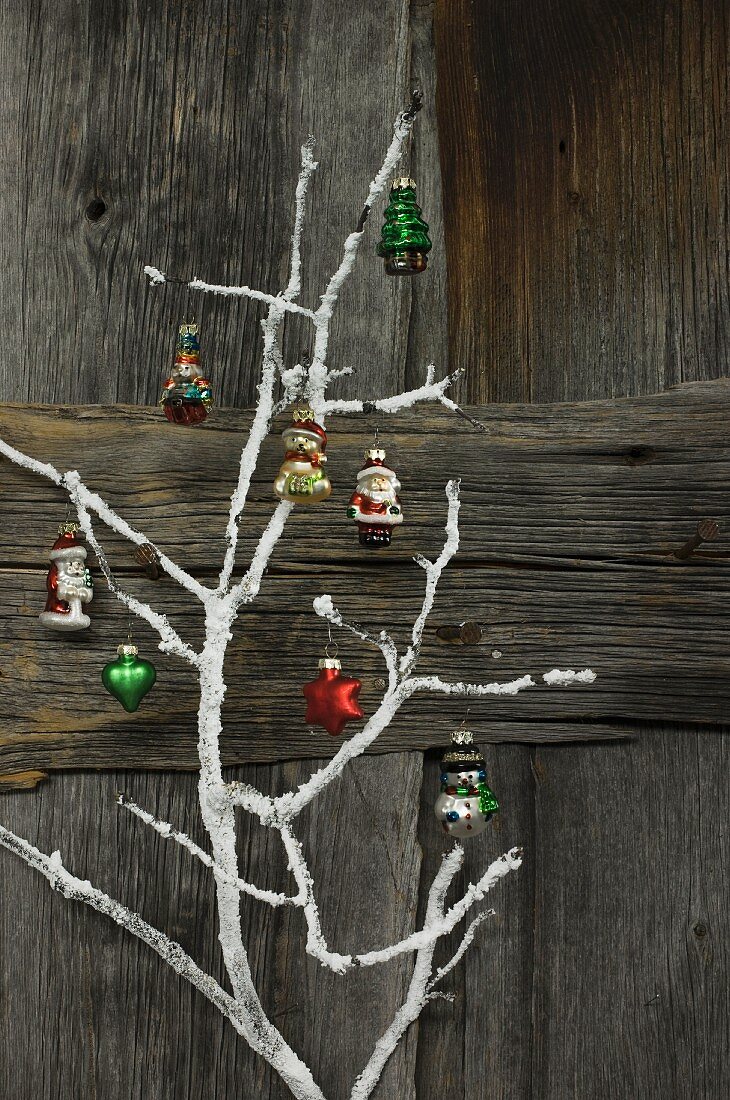 Christmas decorations hung on white-painted branch against rustic wooden wall