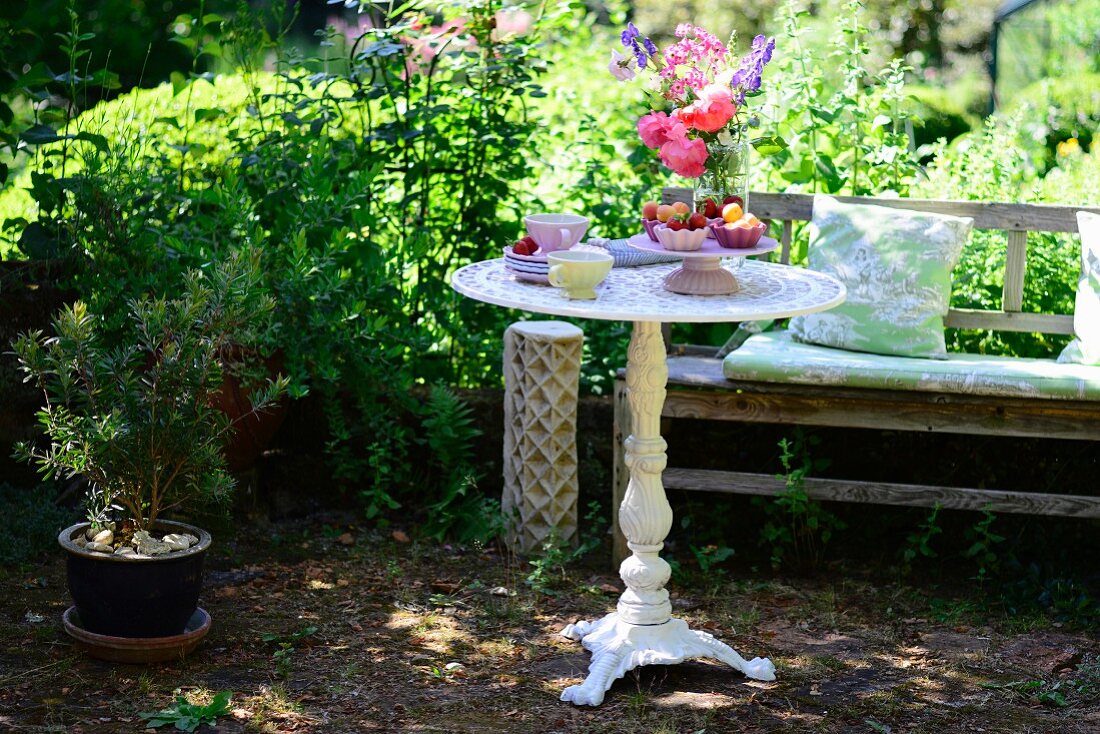 Runder nostalgischer Gartentisch mit Holzbank in sommerlichem Garten