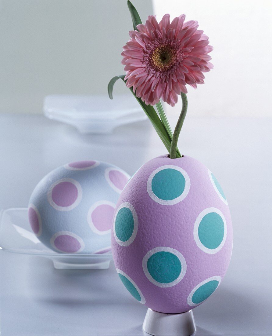 Pink gerbera daisies in egg-shaped vase painted in pastel shades