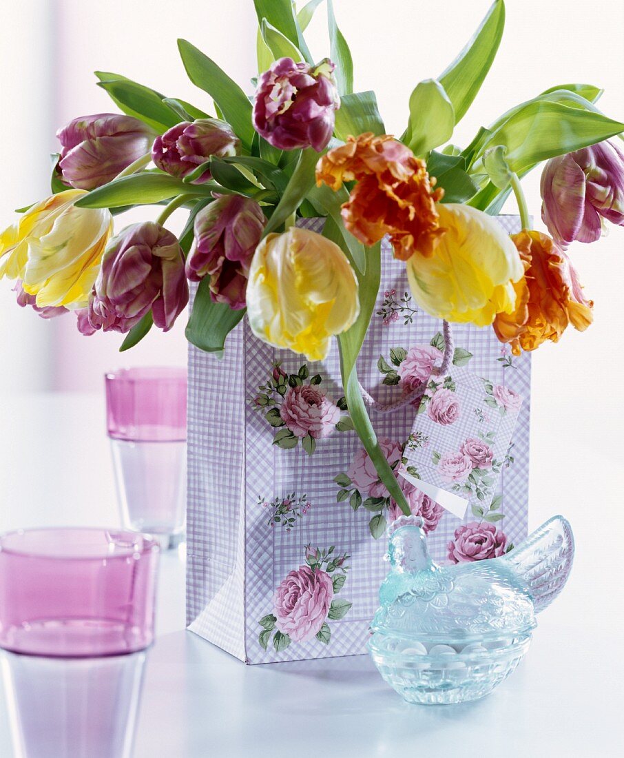 Bouquet of tulips in rose-patterned gift bag and vintage-style hen-shaped glass jar