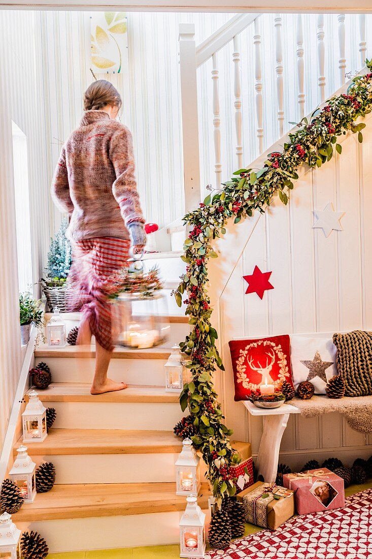 Woman carrying lantern up festively decorated staircase