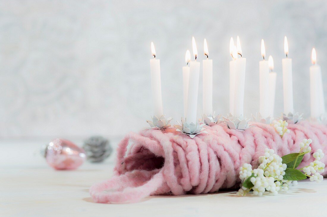 Kleine brennende Kerzen auf einem rosa Knäuel Wolle