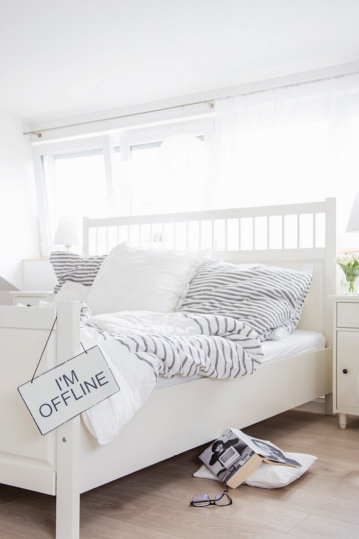 Weisses Doppelbett mit Kopfteil und grau-weiss gestreifter Bettwäsche in Schlafzimmer mit skandinavischem Flair