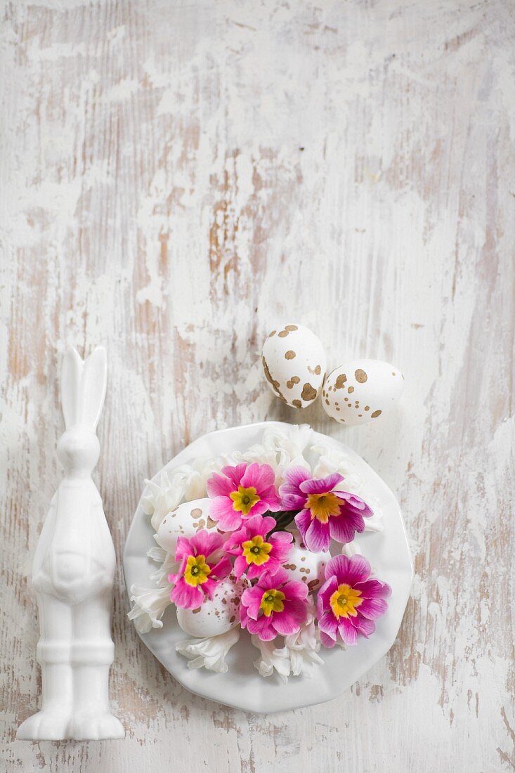 Easter bunny next to plate of flowers and speckled eggs