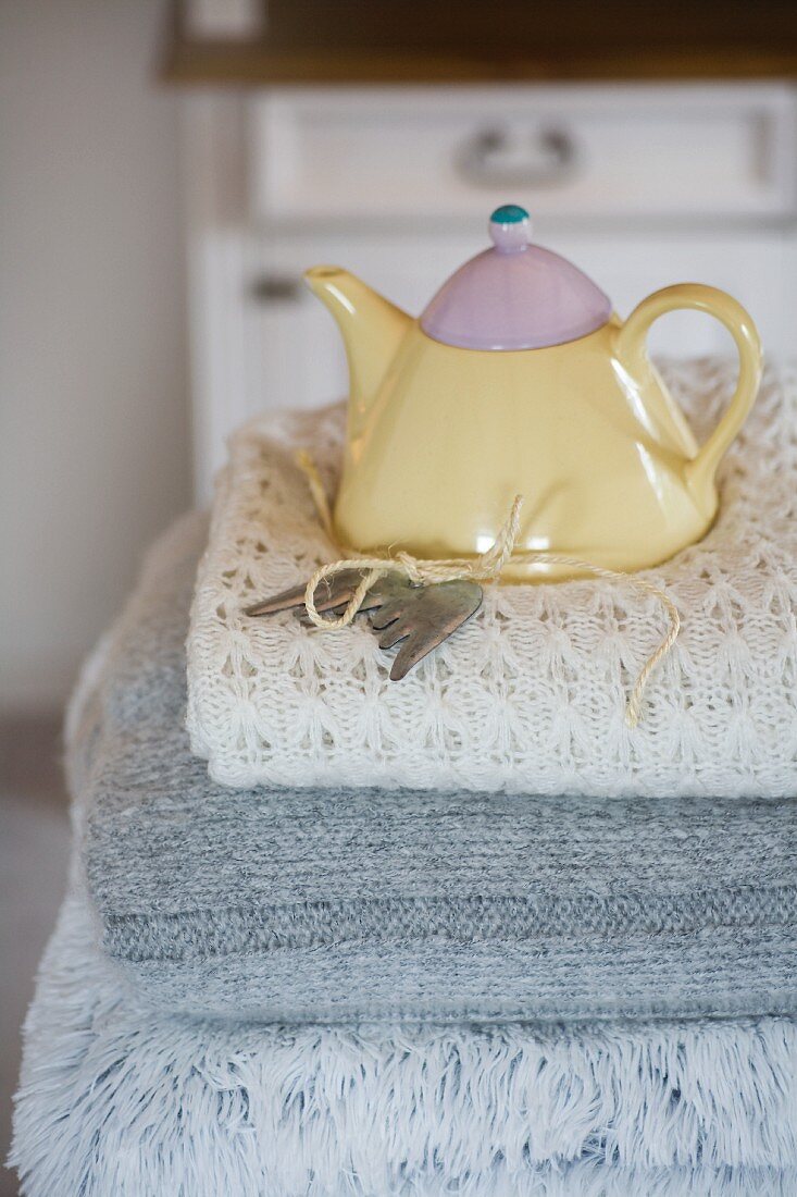 Pastellfarbene Teekanne auf einem Stapel Wolldecken