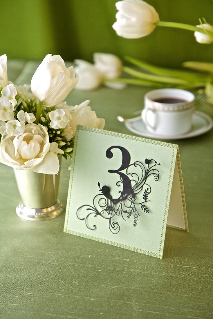 Dekoratives Kärtchen mit der Zahl 3 neben weißem Blumensträusschen auf festlichem Tisch