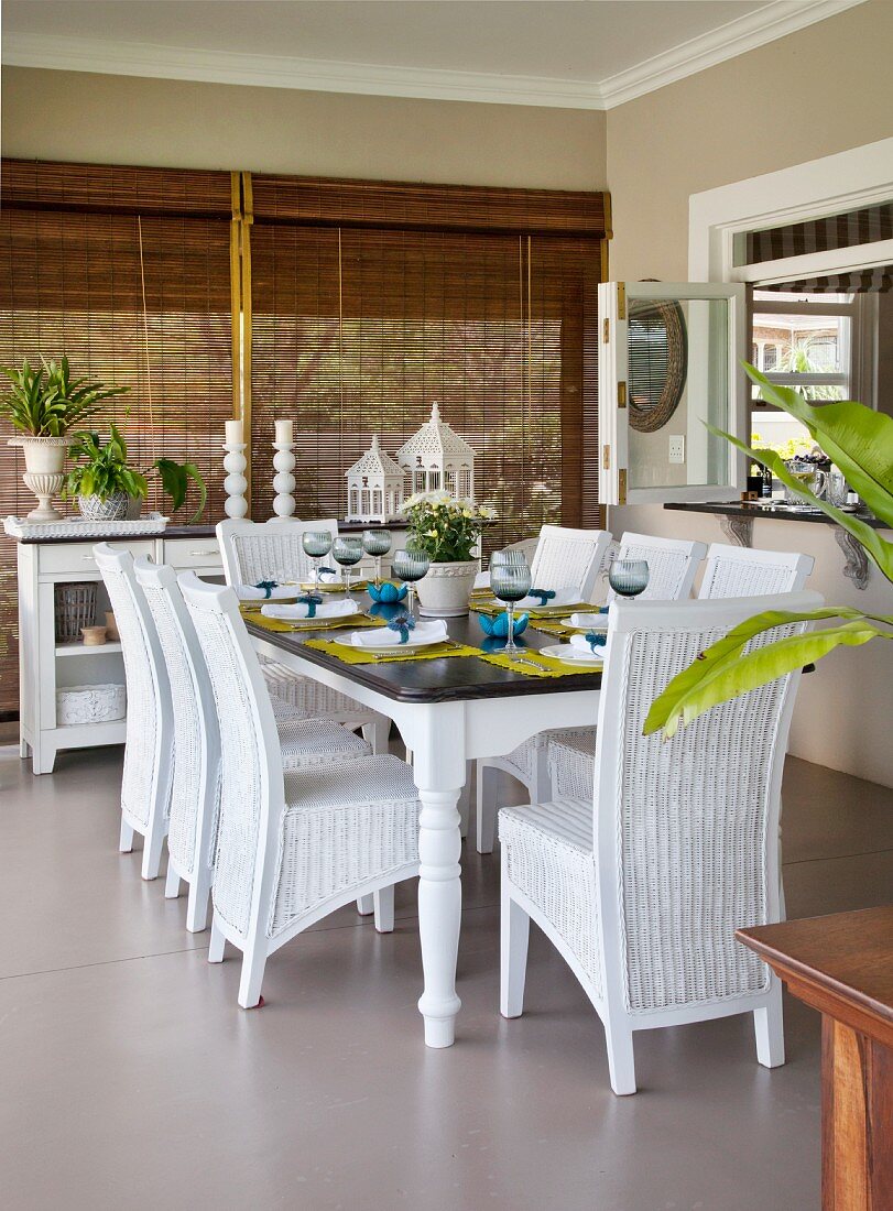 weiße Rattanstühle um gedeckten Tisch in der Loggia, im Hintergrund herunter gelassene Bambusrollos