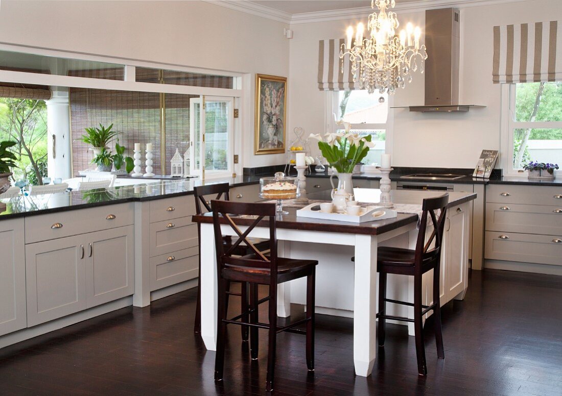 Dark wooden chairs at dining table adjoining counter in kitchen with white, country-house-style cabinets
