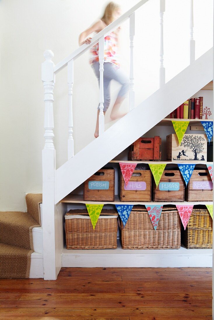 Storage shelves with wooden crates and baskets under white staircase
