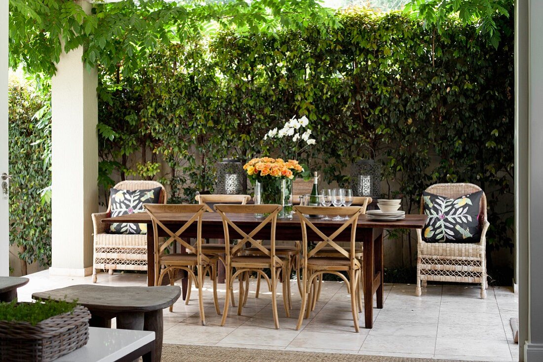 Langer Esstisch und Bugholzstühle, seitlich Rattanstühle auf gefliester sommerlicher Terrasse