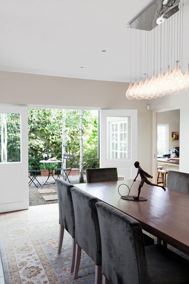 Dining table, dark brown upholstered chairs, designer pendant lamp and open French windows
