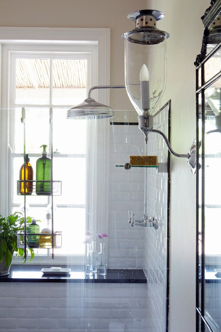 Sconce lamp with glass lampshade next to white-tiled shower area behind glass screen