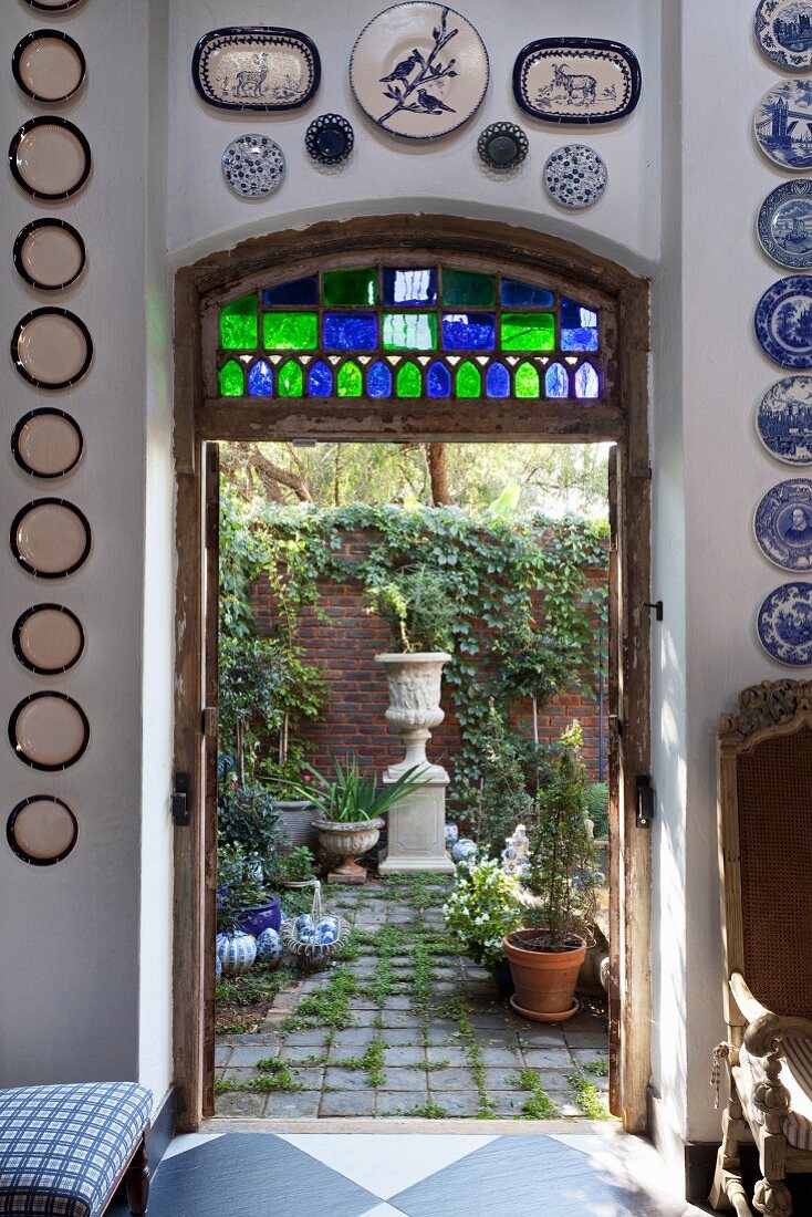 Blick durch offene Tür in den begrünten Hinterhof auf antik griechisches Pflanzengefäss und Ziegelmauer